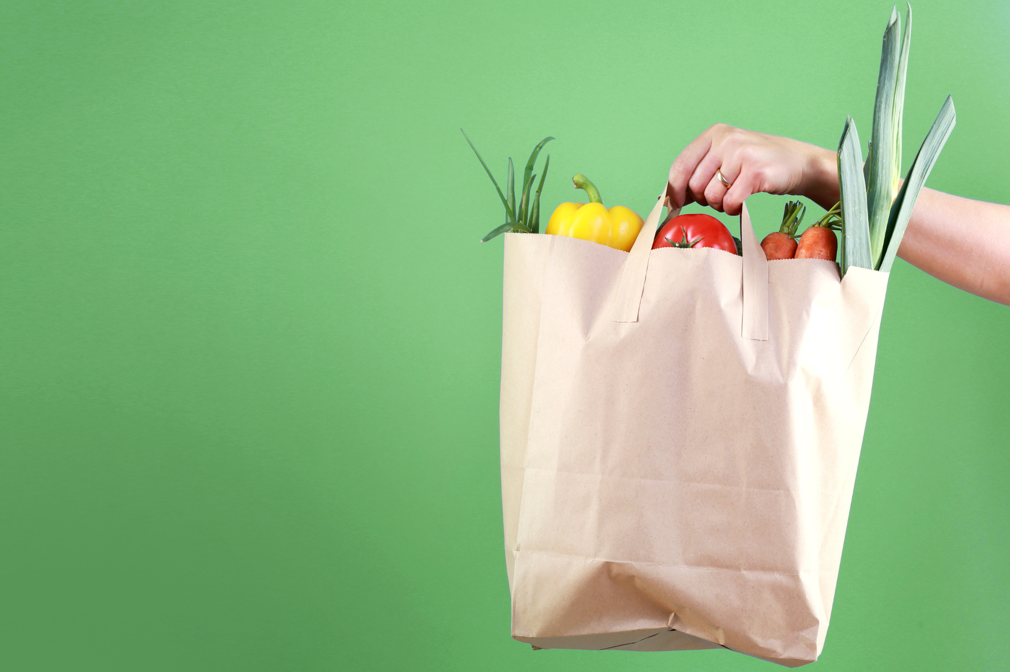 Person holding paper bag filled with groceries against green background